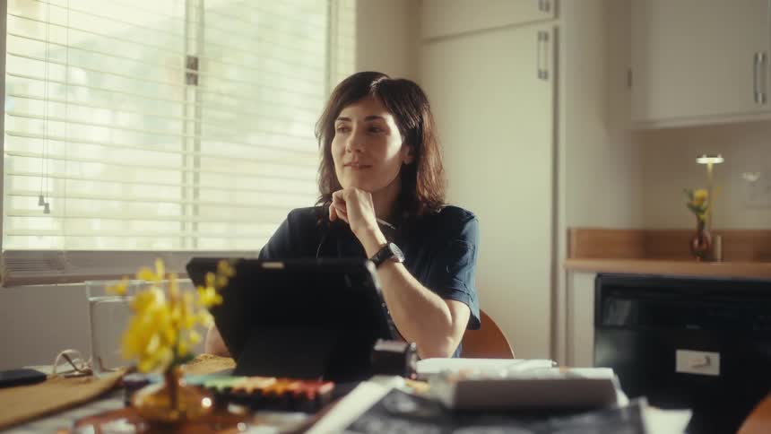 A thoughtful female doctor in scrubs takes a quiet moment of reflection at her sunlit kitchen table