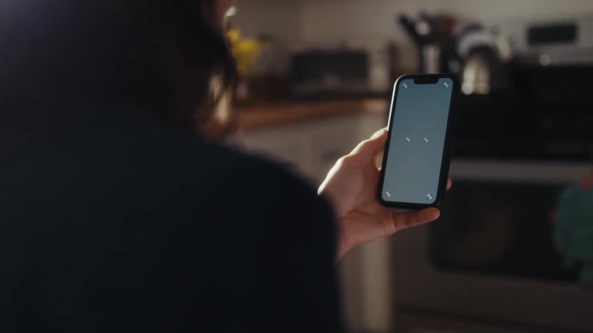 An over-the-shoulder view of a person holding a smartphone with a chroma key screen inside a kitchen