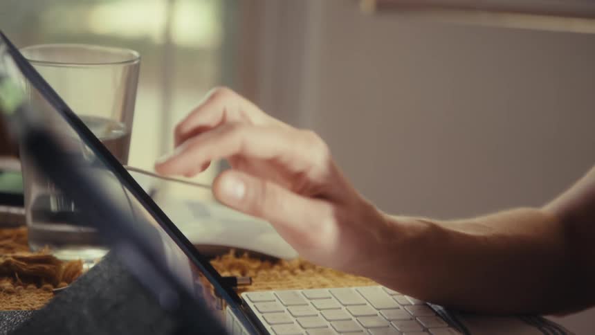 Close-up of a person's hands using a calculator and a tablet computer while working at a desk