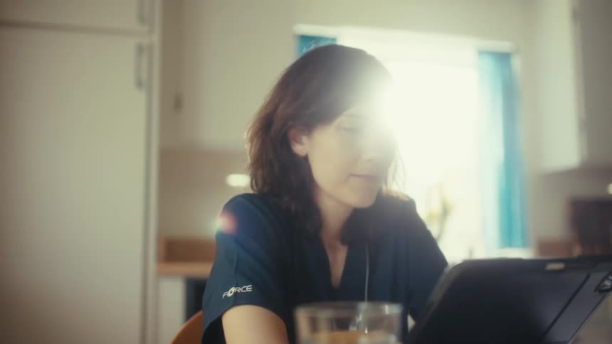 A female medical professional in scrubs uses a tablet and stylus in a sunlit room, with the camera slowly pulling back