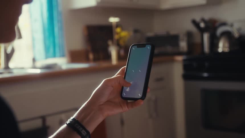 A person scrolls on their smartphone with a screen ready for compositing while sitting in a sunlit kitchen