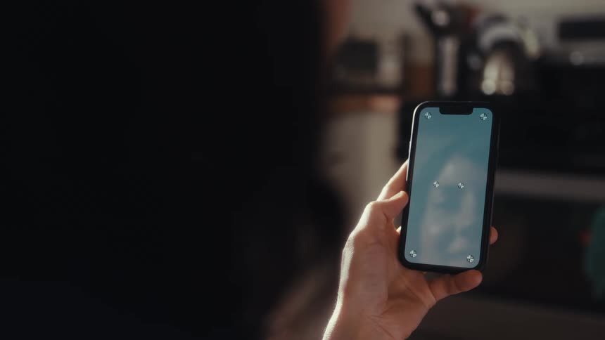 Over-the-shoulder shot of a person holding a smartphone with tracking markers on the screen