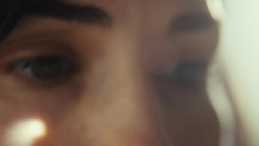 A dreamy extreme close-up of a person's brown eye, slowly shifting focus with a soft lens flare