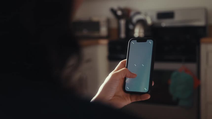 An over-the-shoulder shot of a person holding a smartphone with a screen ready for replacement inside a kitchen