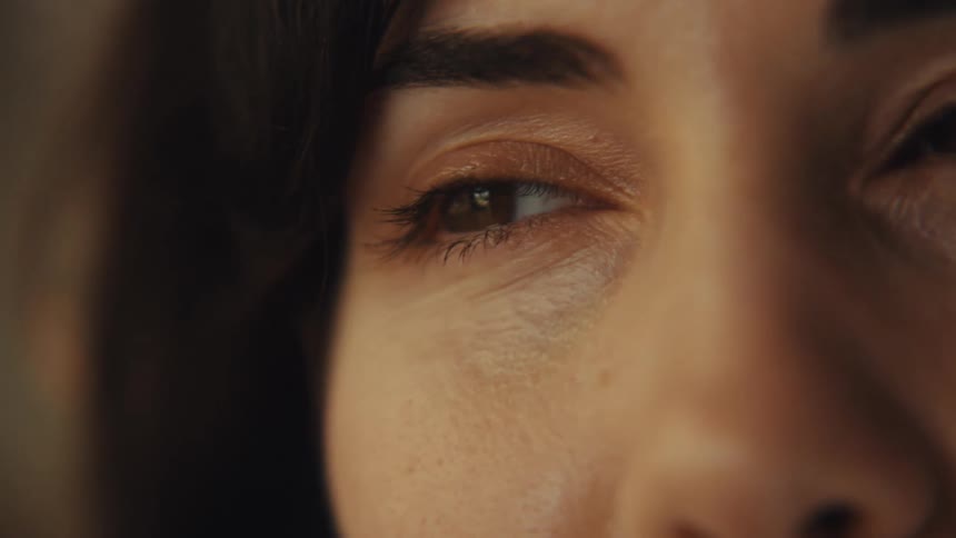 An extreme close-up shot focuses on a woman's brown eyes as she looks off-camera
