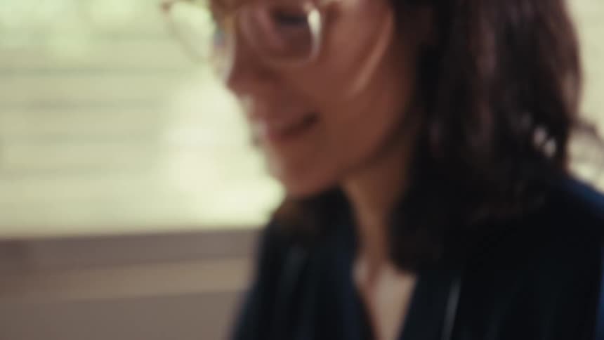 A smiling female doctor in scrubs uses a calculator while reviewing financial charts and documents at her desk