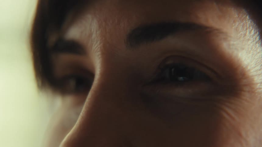 A macro shot of a woman's eye, smiling with wrinkles, then closing and opening slowly in soft, natural light