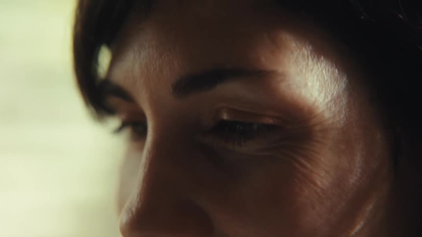 Close-up slow motion shot shows a woman's eye and smiling wrinkles in soft, moody lighting