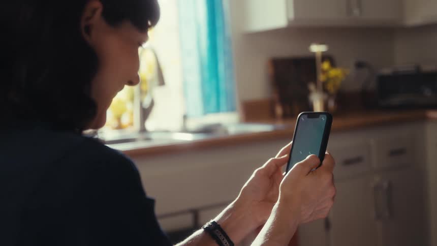 Over the shoulder view of a woman scrolling on her smartphone in a sunlit kitchen