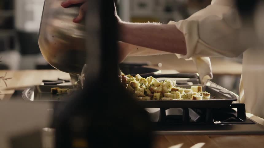 A chef pours herbed croutons onto a baking tray
