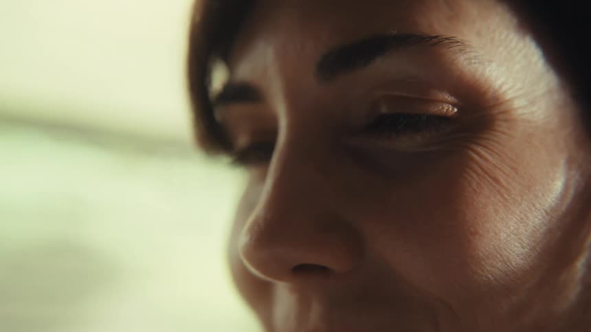 An intimate close-up of a woman's face reveals a gentle smile as the camera tilts up to her eyes, showing wrinkles of happiness