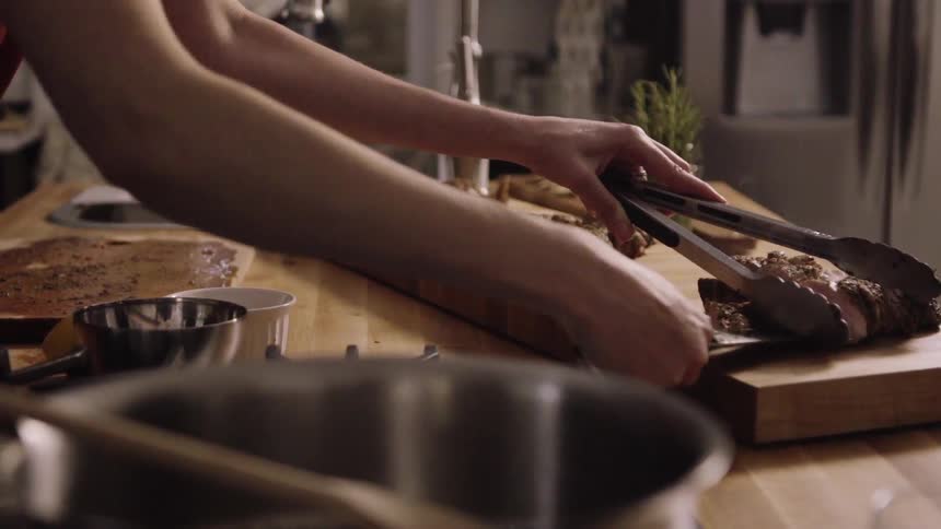 A woman is using tongs and a knife to plate some meat
