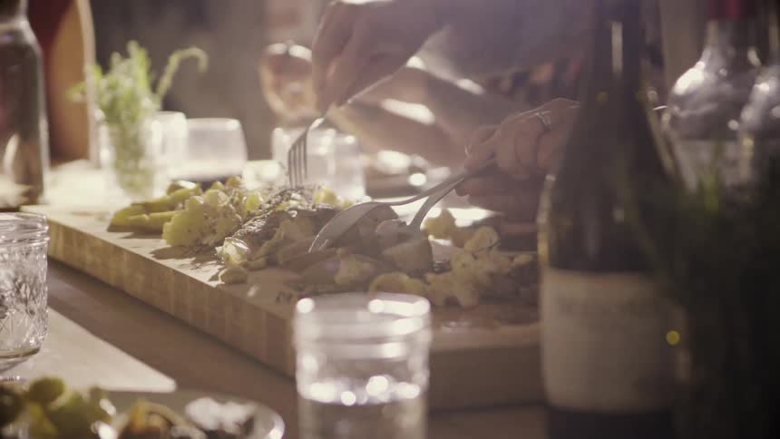 People serve themselves from a platter of food set on a dinner table