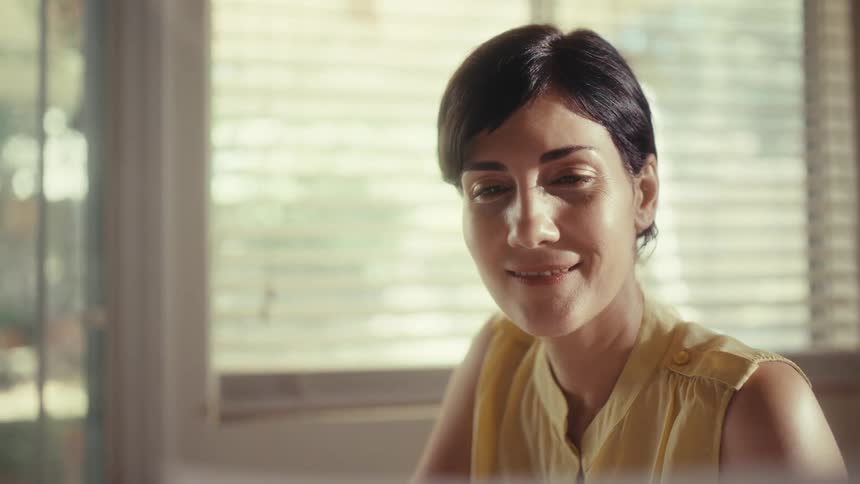 A businesswoman happily analyzes a paper chart while working on her tablet in a naturally lit home office