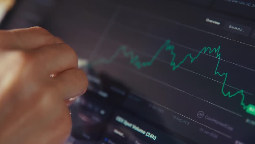 Close-up shot of a hand using a stylus to analyze a fluctuating stock or cryptocurrency chart on a digital tablet