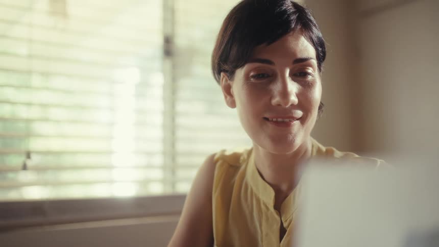 A successful woman happily reviews business performance charts on paper while working from her sunlit home office