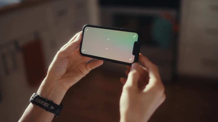 Over-the-shoulder shot of a person holding a smartphone horizontally with a green screen and tracking markers