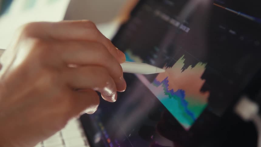 A close-up of a person's hand using a digital stylus to analyze a colorful financial graph on a tablet screen