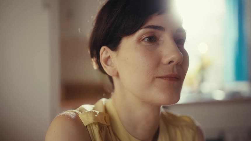 Close-up portrait of a thoughtful woman with a gentle smile, beautifully lit by a sun flare from a nearby window