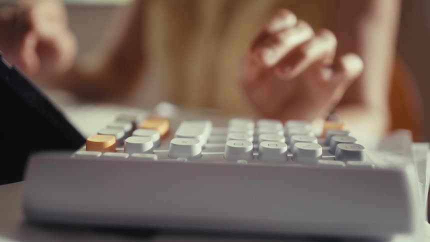 A close-up shot focuses on a person's hand as they use a modern calculator to work on their finances