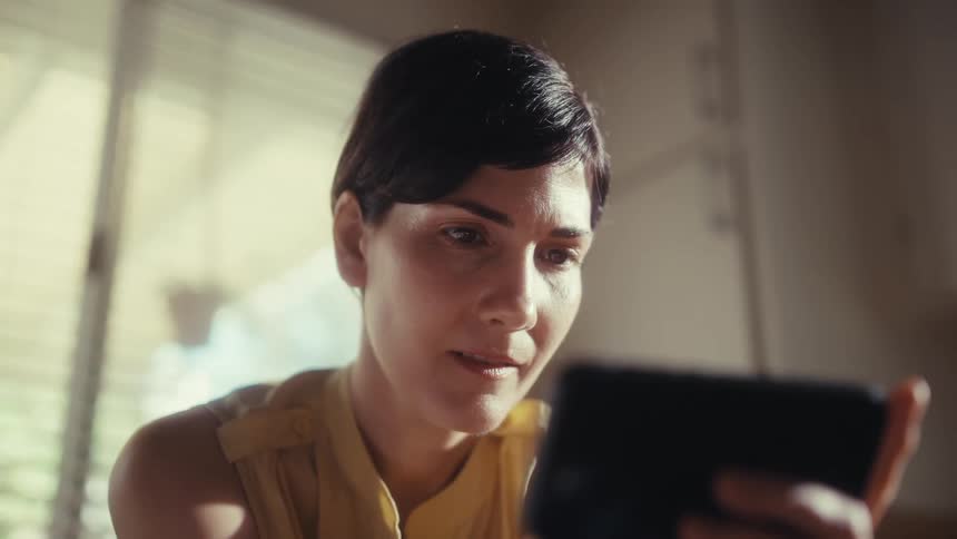 Close up of a professional woman with short dark hair watching something on her phone in a dimly lit office