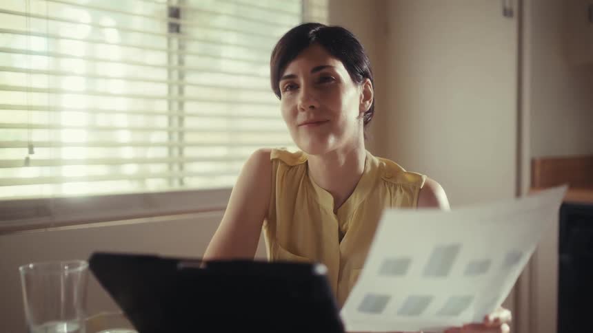 A focused businesswoman works remotely from her kitchen, smiling with satisfaction as she reviews positive business charts and data
