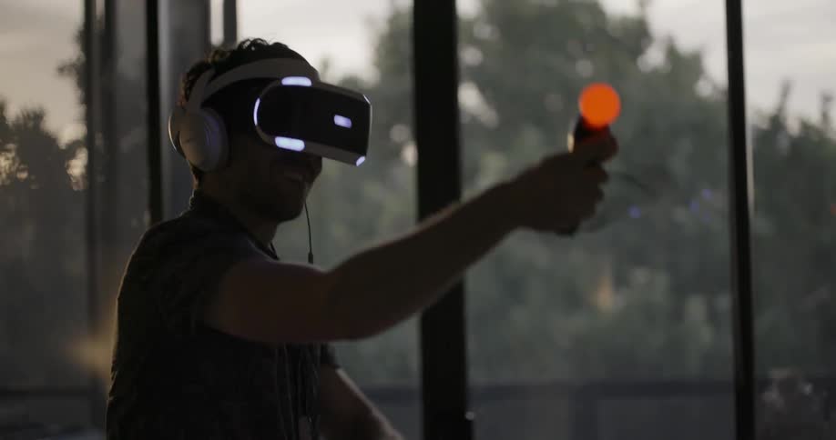 A man is swinging controllers playing virtual reality at sunset