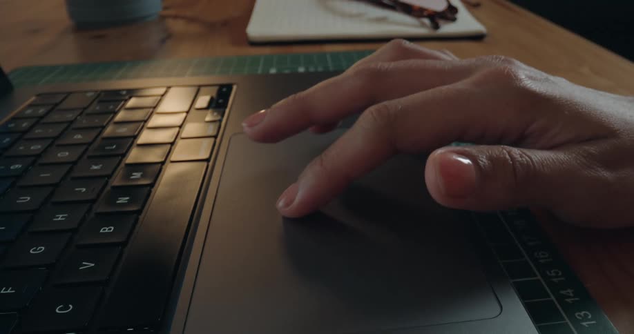 A close-up view of a manicured hand using the trackpad of a laptop computer on a desk