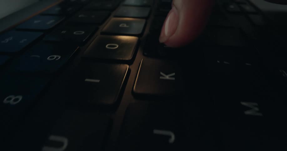 Extreme close-up slow-motion dolly shot of fingers typing on a dark laptop keyboard