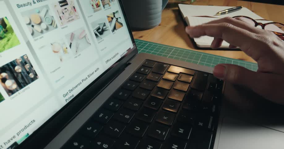 A close-up shot of hands scrolling through an online shopping website on a laptop at a desk