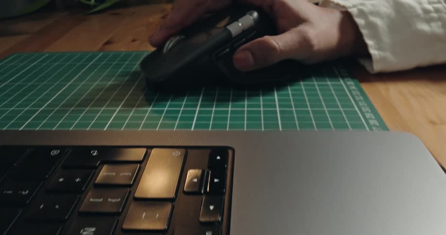 A close-up slow dolly shot reveals a hand using a wireless computer mouse on a desk next to a laptop