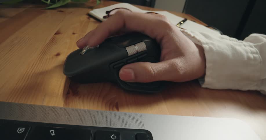 A close-up shot slides past a laptop keyboard to reveal a hand scrolling and clicking a modern ergonomic mouse on a desk