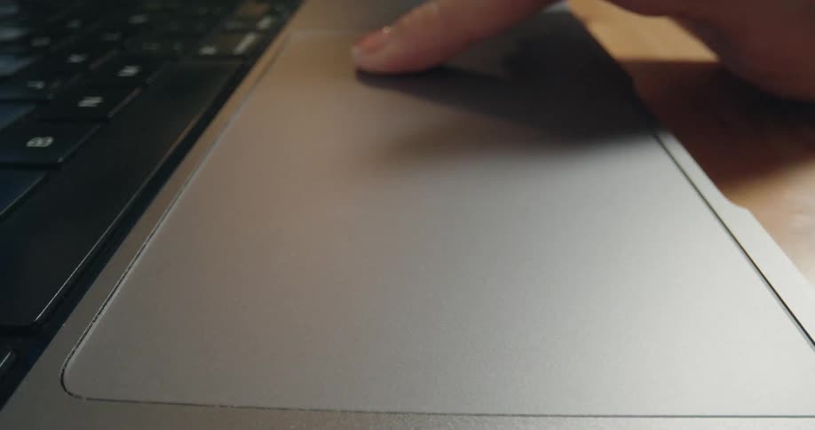 A close-up view of a person's finger tapping and scrolling on a modern laptop trackpad