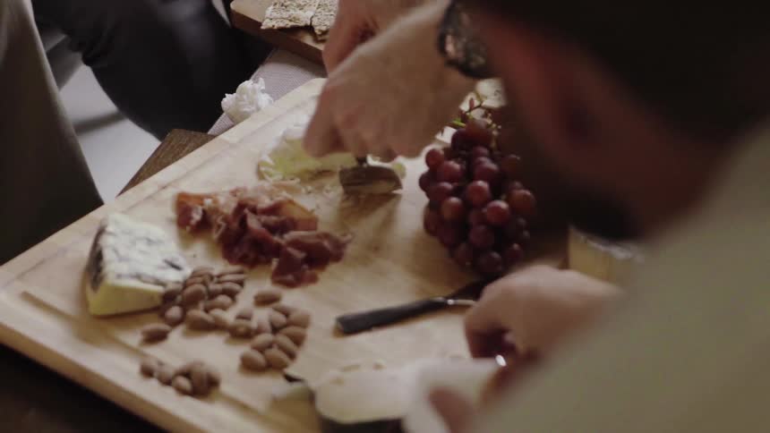 A man scoops up a bit of cheese from a selection of food onto a cracker