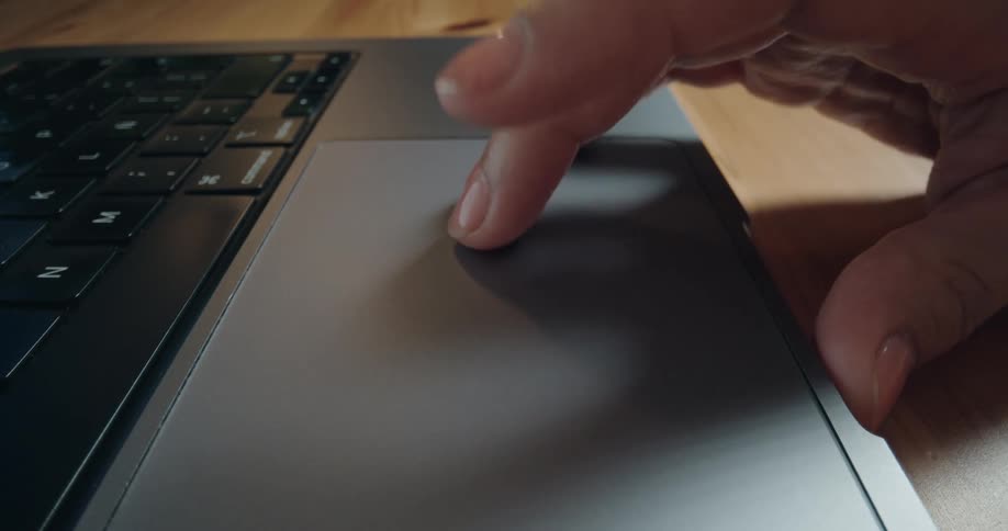 A macro close-up shot pans across a laptop keyboard to a hand resting on the trackpad