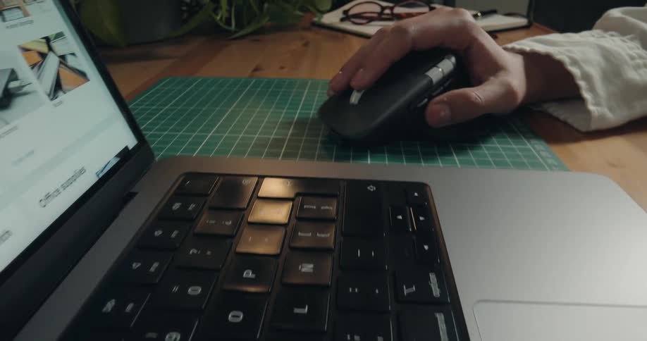 Close-up dolly shot of a person browsing an online store on a laptop using a wireless mouse