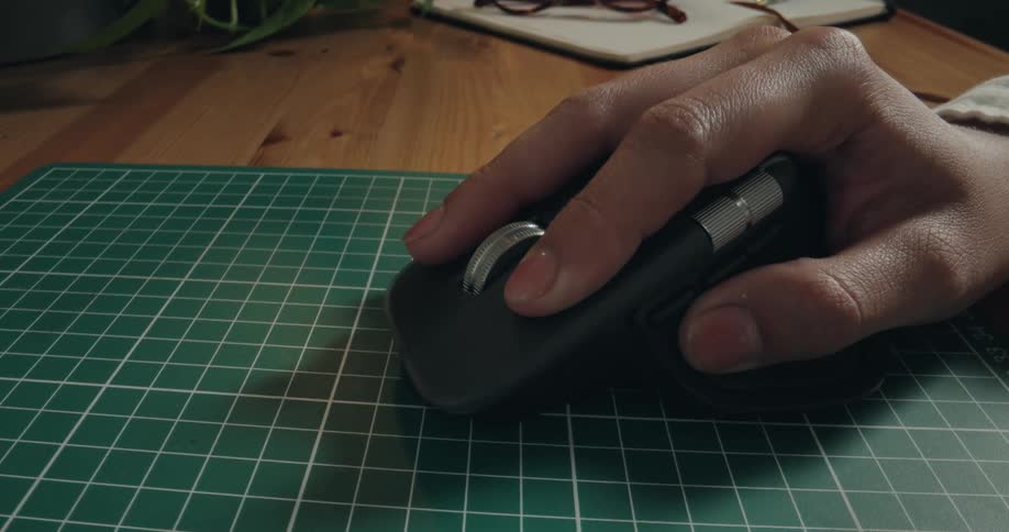 A dynamic push-in shot reveals a close-up of a hand using a wireless mouse on a gridded mat next to a laptop