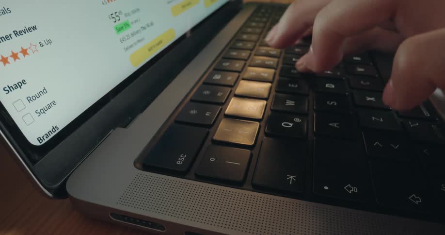 A close-up of hands typing on a laptop keyboard while browsing an e-commerce website for online shopping