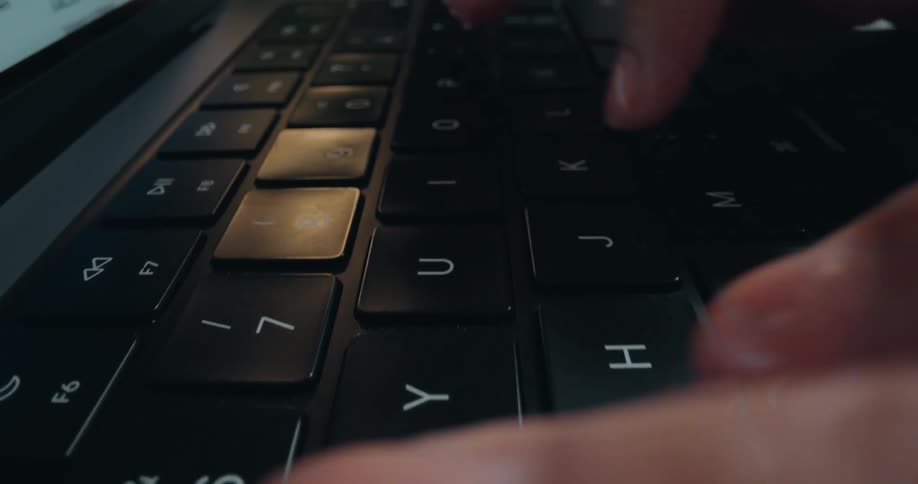 A dramatic extreme close-up of a person's fingers quickly typing on a modern black laptop keyboard