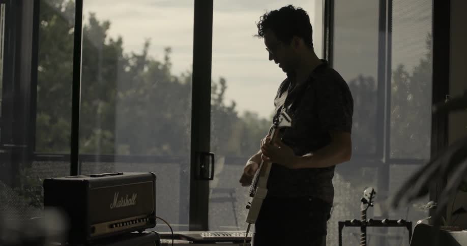A man is playing a guitar as he stands in a room