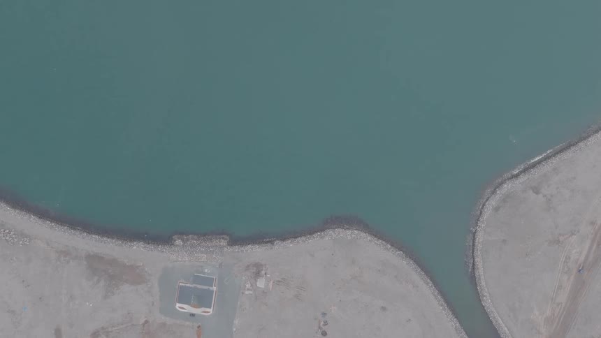 Aerial top-down view of a desolate coastline where a van arrives and a person gets out next to the calm, green water