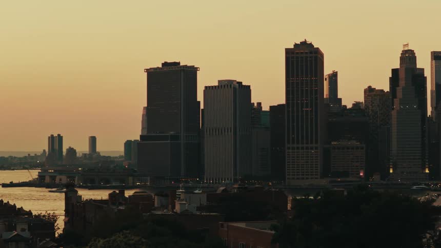 Golden hour sunset over the Manhattan skyline, with skyscrapers silhouetted against the warm sky and the river below