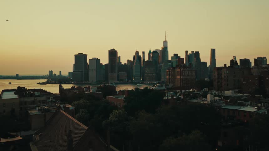 An aerial view slowly pushing in on the iconic Manhattan skyline at golden hour, as seen from across the East River in Brooklyn