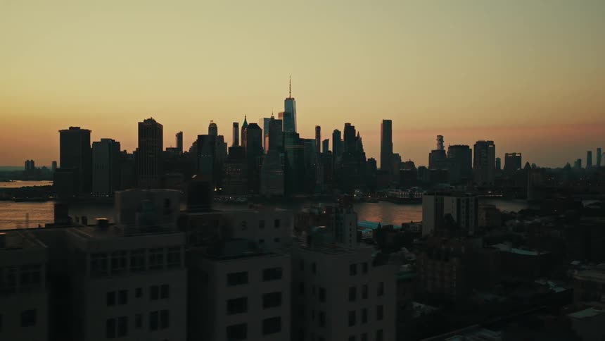 An aerial dolly shot pulls back to reveal the iconic New York City skyline silhouetted against a beautiful sunset sky over the East River