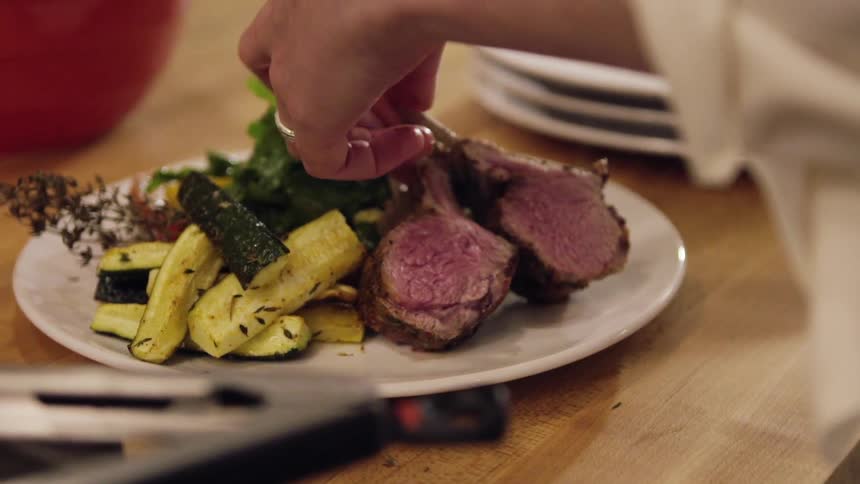 Person places meat onto a plate with vegetables and picks it up