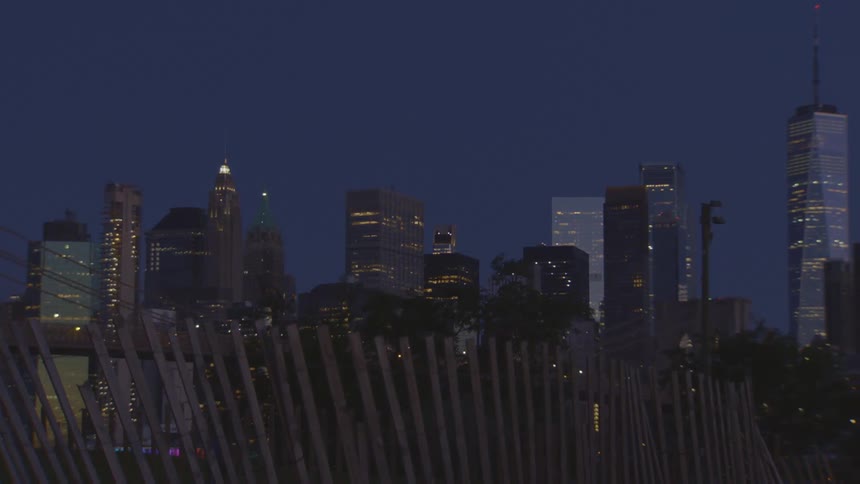 The iconic Manhattan skyline and Freedom Tower are illuminated at dusk as seen from across the water