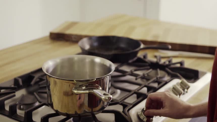 Person turns a stove on with a pot on the burner