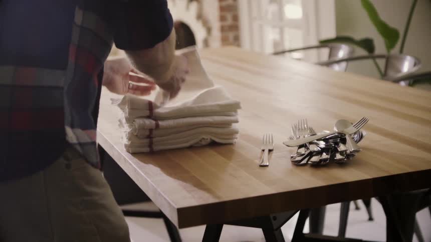 A man puts napkins and cutlery on a dining table