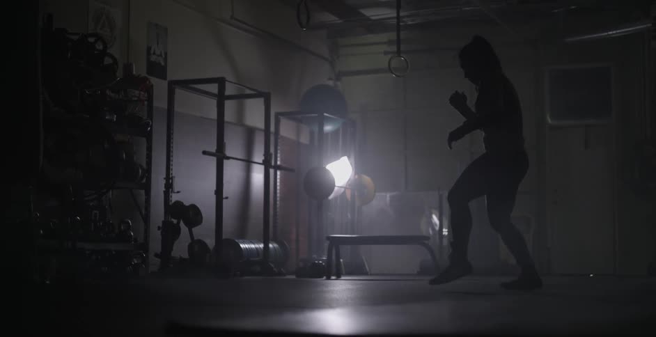 Woman jumps and waves arms in a dimly lit gym
