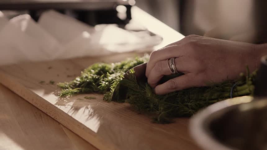 A woman is cutting greens on a board